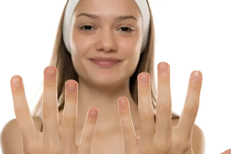 Une jeune femme souriante montre son ongle transparent